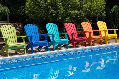 Light Blue, Dark blue, Yellow, Green Red and Orange COMFO BACK STATIONARY ADIRONDACK CHAIRS beside a pool